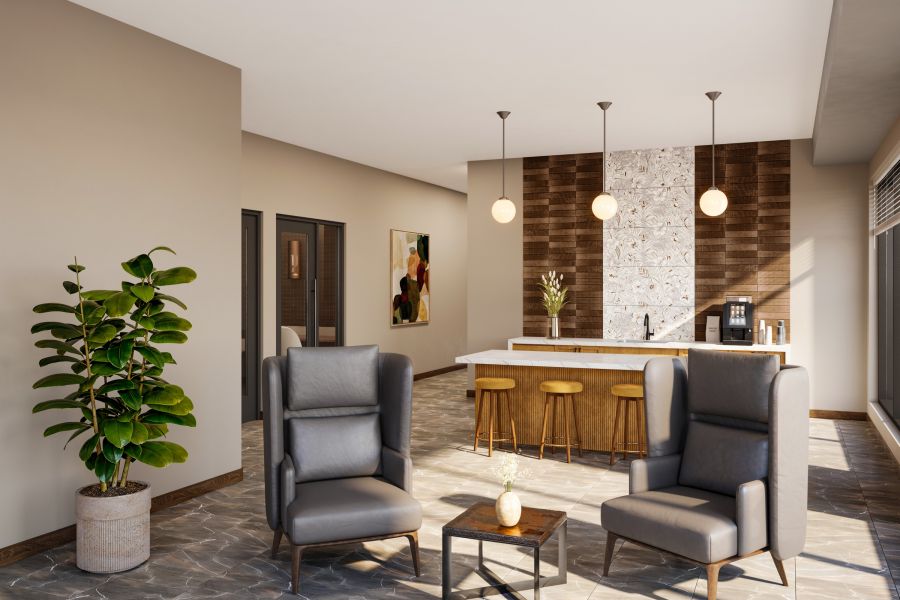 Modern lounge with two gray armchairs, a small table, a potted plant, and a kitchen island in the background.