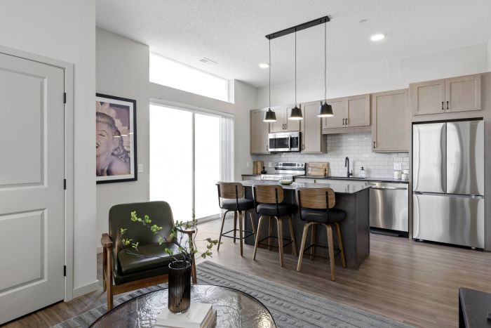 Modern kitchen and living area with bar stools, stainless steel appliances, and a framed portrait on the wall.