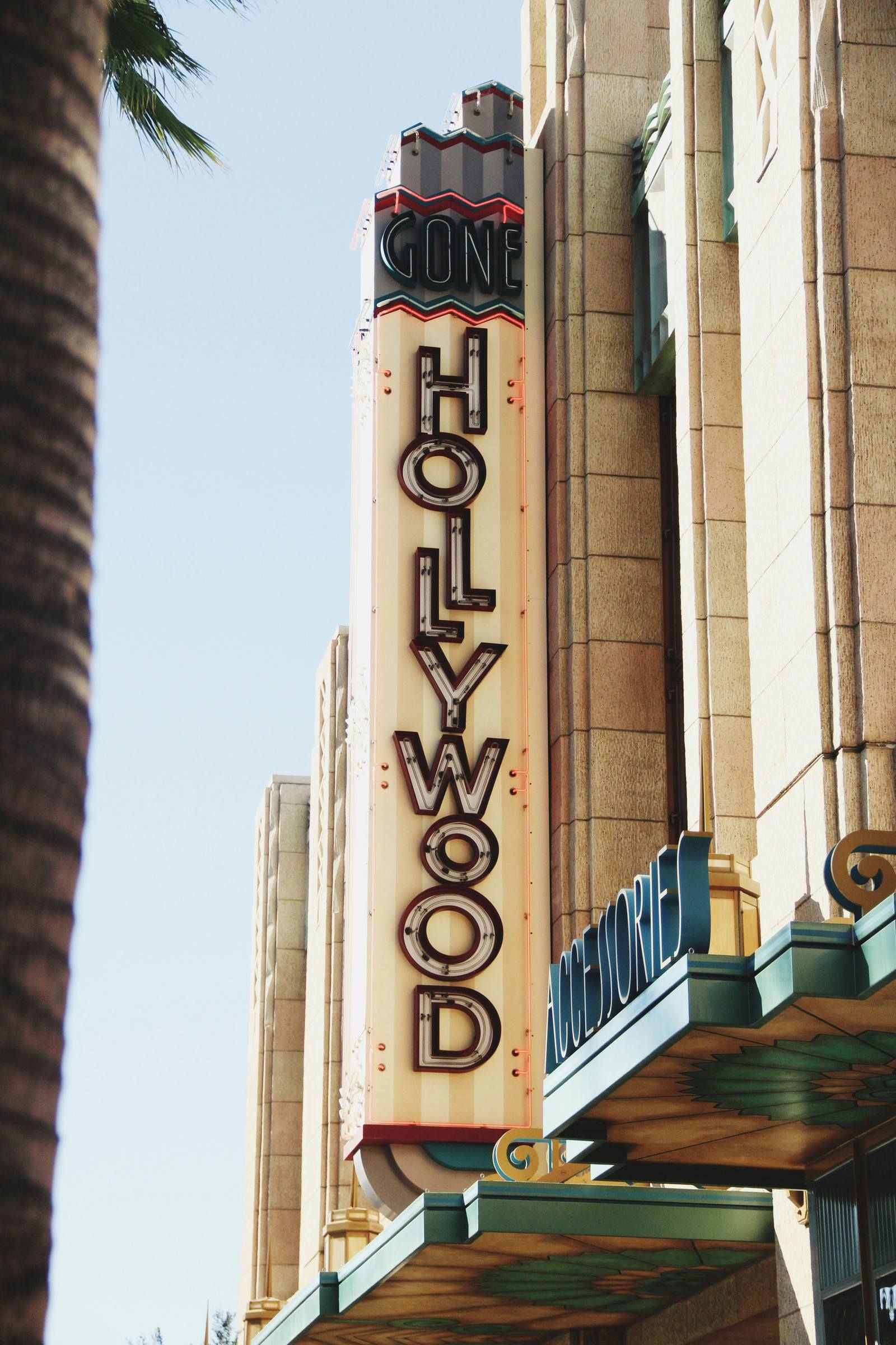 Vertical "Hollywood" theater sign on art deco building, with "Gone" above and palm tree partially visible on left.